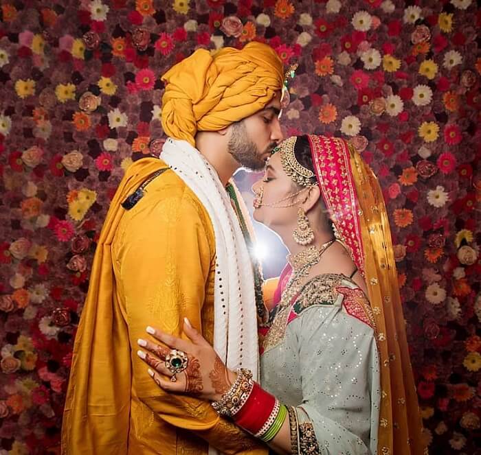Young Indian Bride groom posing for photograph. Groom kissing the forehead  of bride. The couple is wearing traditional indian wedding dress which is  designer lehenga for bride and sherwani for groom. Stock
